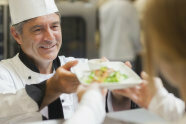 Koch reicht einen Teller mit Essen